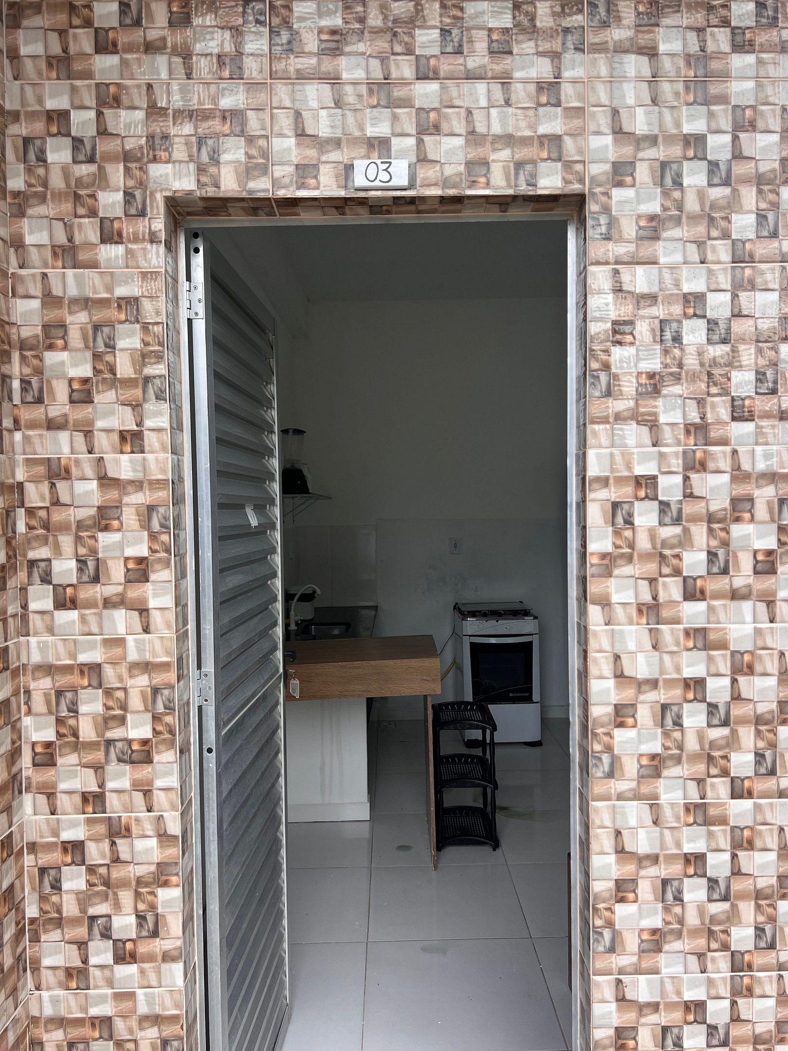 Een kamer met een betegelde muur, een houten toonbank, een kleine zwarte stoel en een wit apparaat.