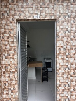 Una habitación con pared de azulejos, mostrador de madera, una pequeña silla negra y un electrodoméstico blanco.