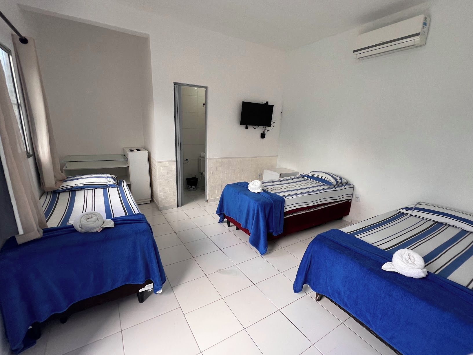 A hotel room with three beds, a TV, and an air conditioning unit.