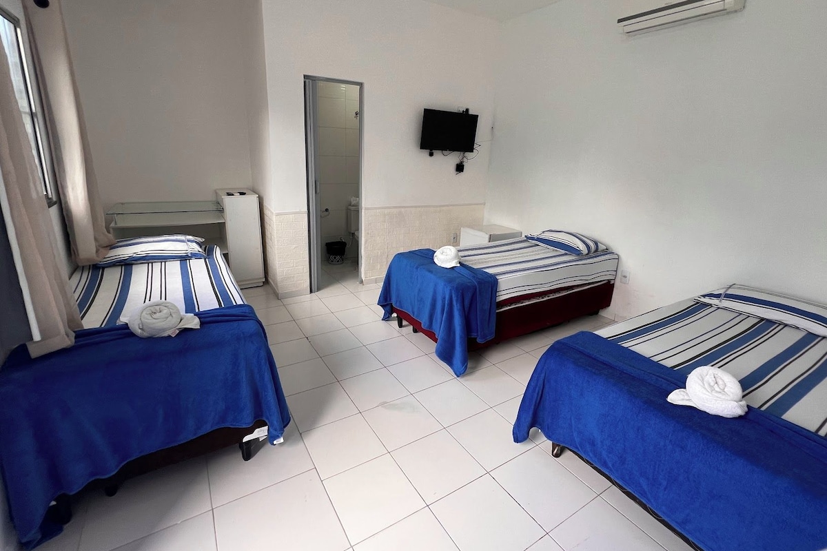 Habitación de hotel con tres camas, televisión y aire acondicionado.