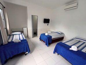Habitación de hotel con tres camas, televisión y aire acondicionado.