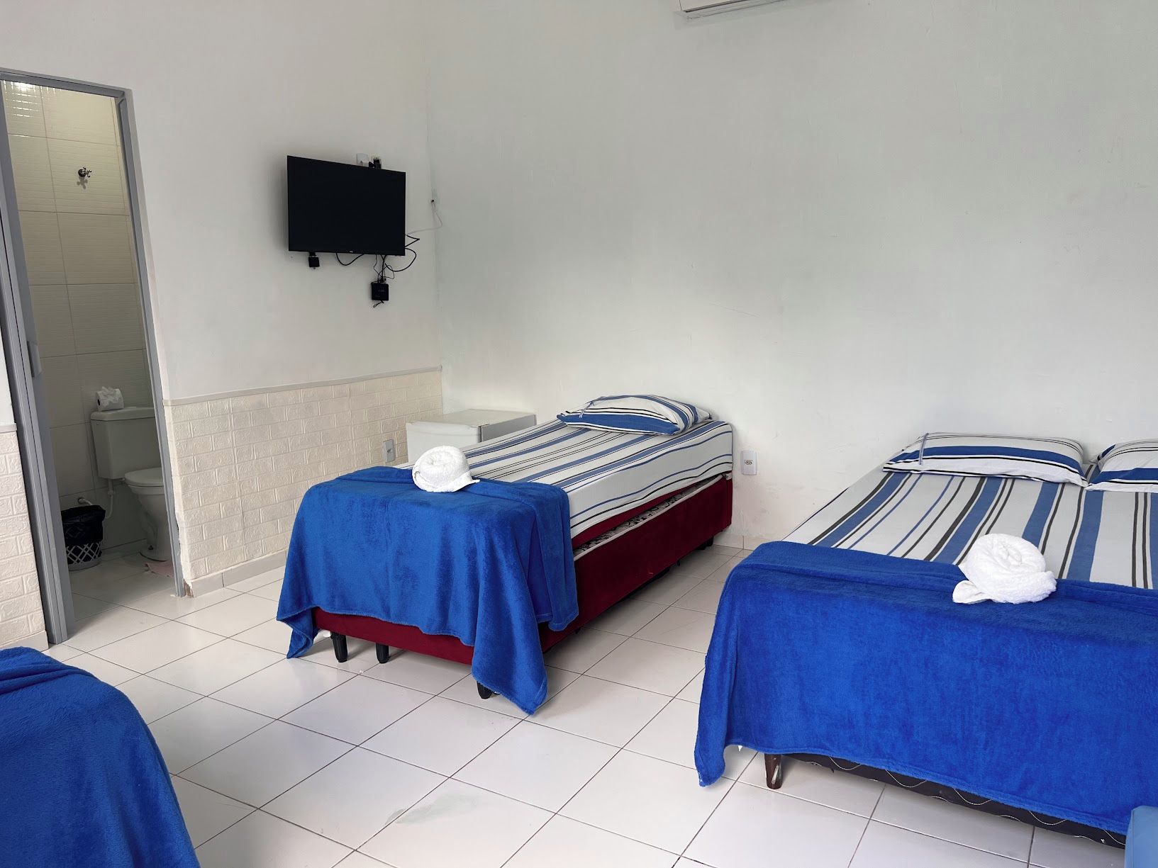 A hotel room with two beds, a television mounted on the wall, and a bathroom visible through an open door.
