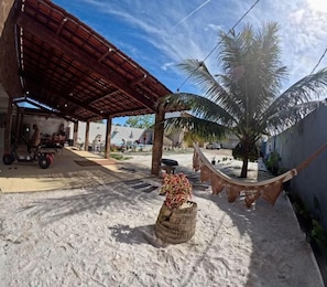 Un espacio al aire libre techado con una hamaca, una palmera y un vehículo.