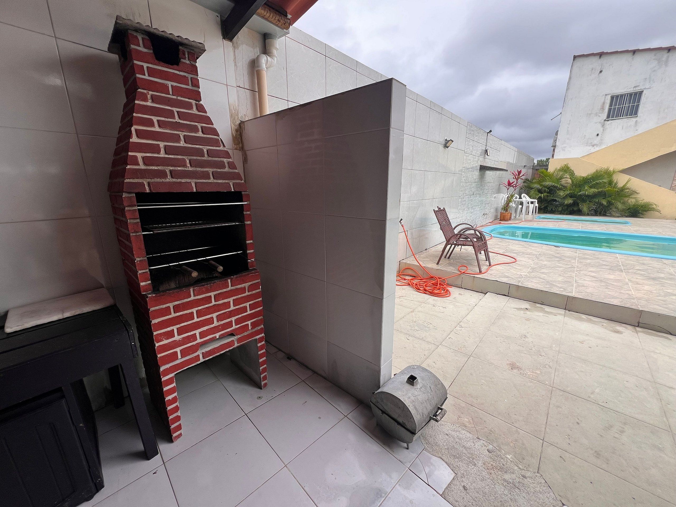 Uma churrasqueira de tijolos, uma piscina e um espaço de estar no pátio com cadeiras.