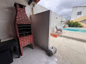 Una parrilla de ladrillo, una piscina y un patio con sillas.