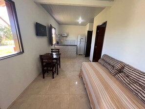 A compact living space with a kitchenette, a dining area with a table and chairs, and a bed with a striped bedspread.