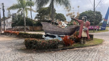 Estátua de um homem segurando um barco, cercada por plantas tropicais e um caminho de pedras.