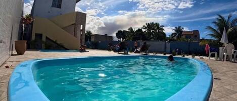 A swimming pool with a curved edge, surrounded by a tiled patio.