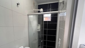 Un baño con inodoro blanco, cabina de ducha con mampara de vidrio y lavamanos blanco.