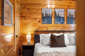 Een houten kamer met een bed, nachtkastje en wanddecoratie met boslandschappen.