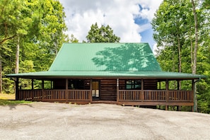 Eine Hütte mit einem grünen Dach, einer Holzfassade und einer Veranda mit Geländern.
