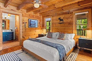 Een slaapkamer in een houten chalet, met een bed, nachtkastjes, een dressoir en een plafondventilator.