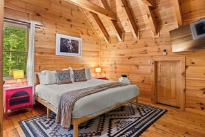 Ein Schlafzimmer einer Holzhütte mit einem Bett, Nachttischlampen, einem gerahmten Foto und einer Tür.