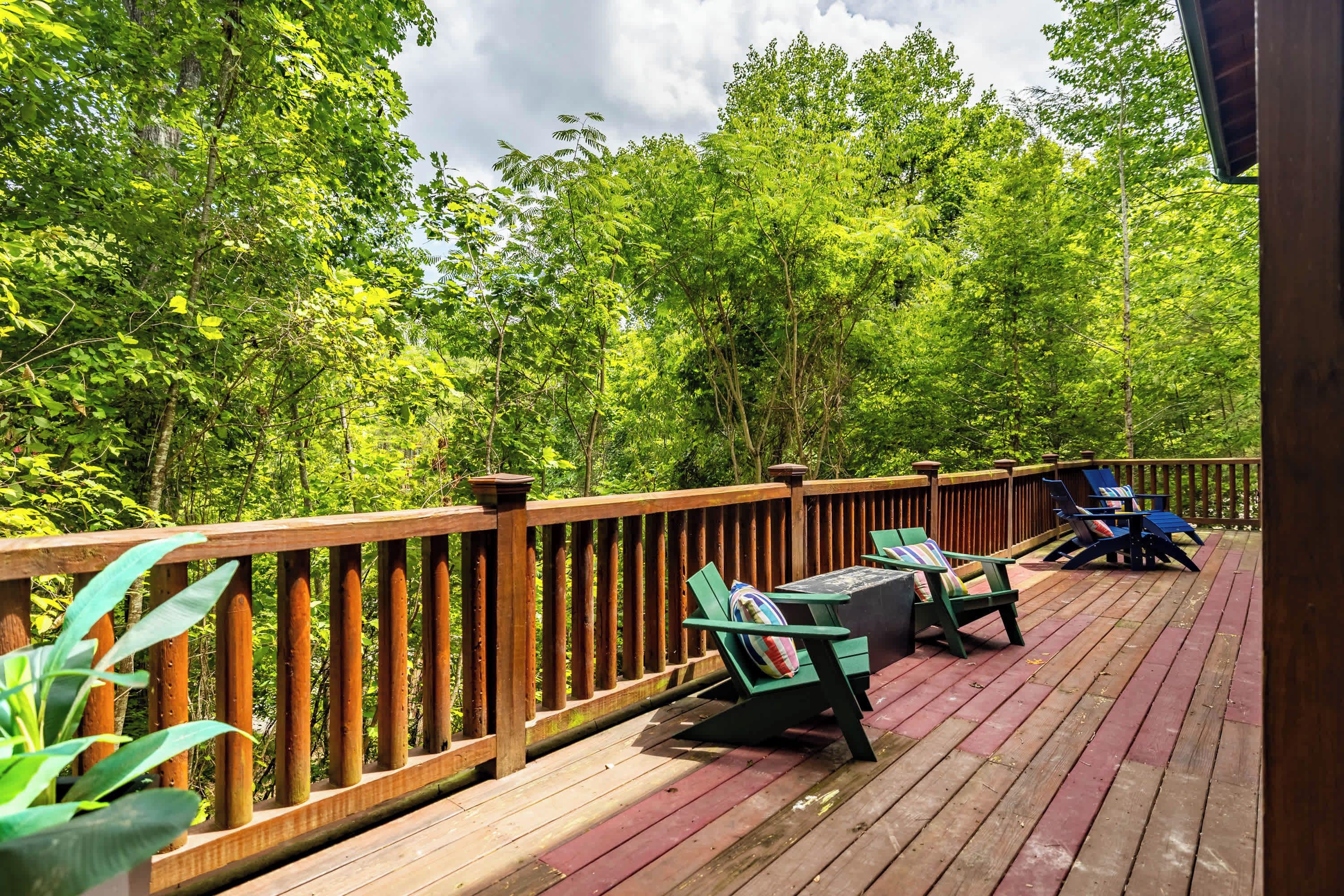 A wooden deck with outdoor furniture, surrounded by dense green foliage.