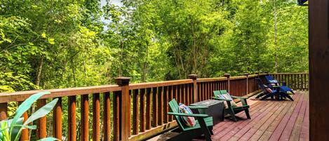 A wooden deck with outdoor furniture, surrounded by dense green foliage.