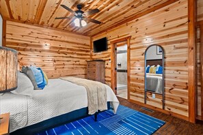 A wooden-paneled room with a bed, a television, and a mirror. - 6BR Smoky Mountain Cabin | Private Indoor Pool, Hot Tub, Theater & 6 Ensuite Baths (Sevierville)