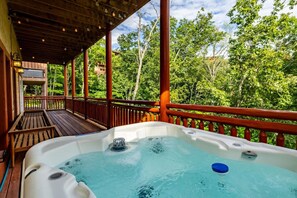 A hot tub on a wooden deck with a view of trees. - 6BR Smoky Mountain Cabin | Private Indoor Pool, Hot Tub, Theater & 6 Ensuite Baths (Sevierville)