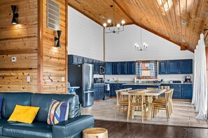 A modern kitchen with dark blue cabinets, a stainless steel refrigerator, and a dining area with wooden chairs and a table. - 6 Ensuite Bedrooms | Private Indoor Heated Pool, Theater, Hot Tub & Mountain Views (Sevierville)