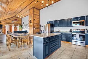 A modern kitchen with dark cabinets, stainless steel appliances, and a large island with seating. - Luxury Log Cabin | Indoor Pool |Game Room |Theater (Sevierville)