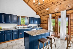 A kitchen with dark blue cabinets, a granite countertop, and a large island with stools. - 6 Ensuite Bedrooms | Private Indoor Heated Pool, Theater, Hot Tub & Mountain Views (Sevierville)