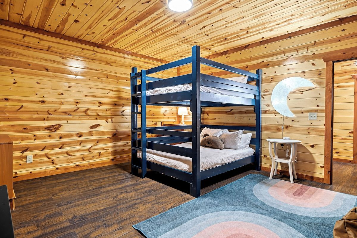 A bunk bed in a wooden cabin room with a circular wall decoration and a small table.