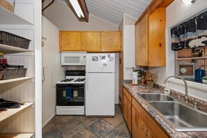 A compact kitchen with wooden cabinets, a white refrigerator, a microwave, a stove, and a sink. - Pine Bear Cabin Cabin W Hot Tub (Big Bear)