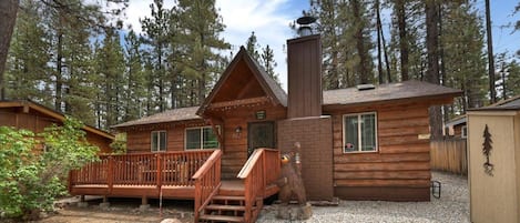 Une cabane dotée d’une terrasse en bois, d’une cheminée et d’un foyer en pierre.