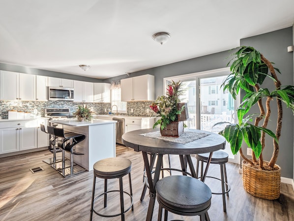A modern kitchen with white cabinets, a central island, and a dining area with stools.