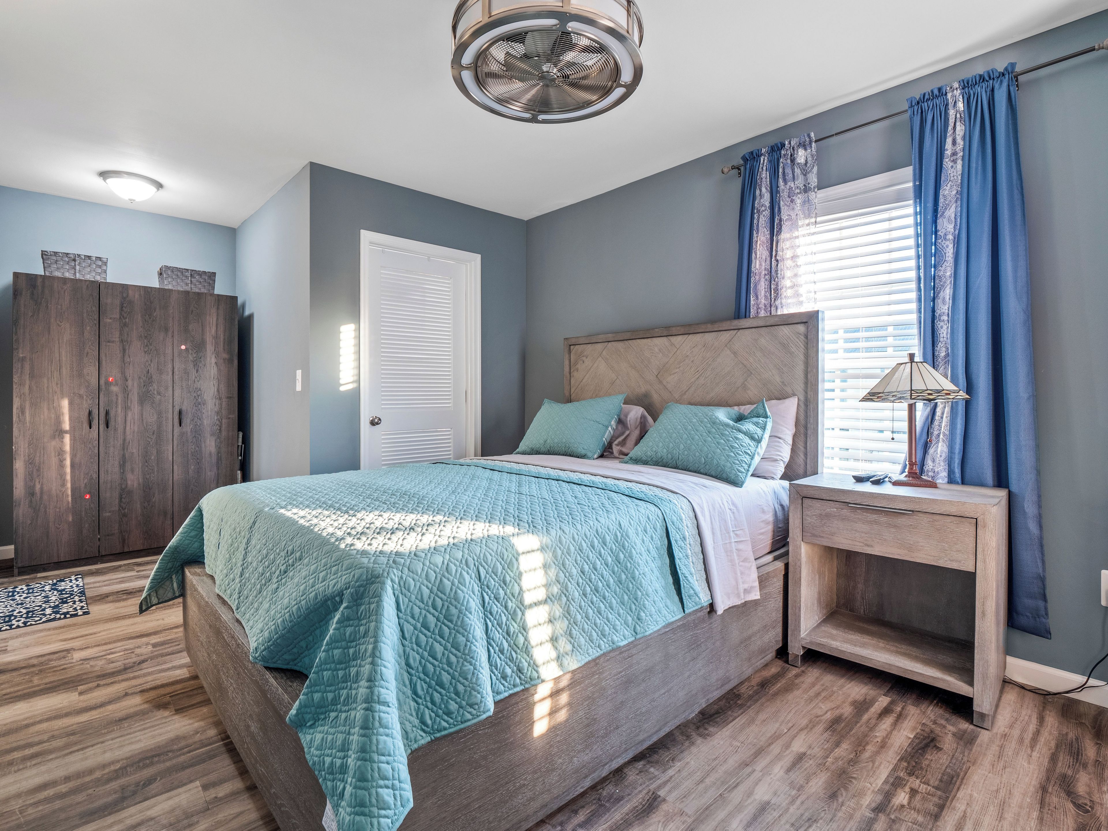 A bedroom with a bed, a nightstand, a wardrobe, and a ceiling fan.