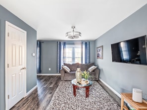 A living room with a grey sofa, a coffee table, and a television on the wall. - Valclyde Capitol 2BR Retreat with Balcony & Free Parking (Washington)