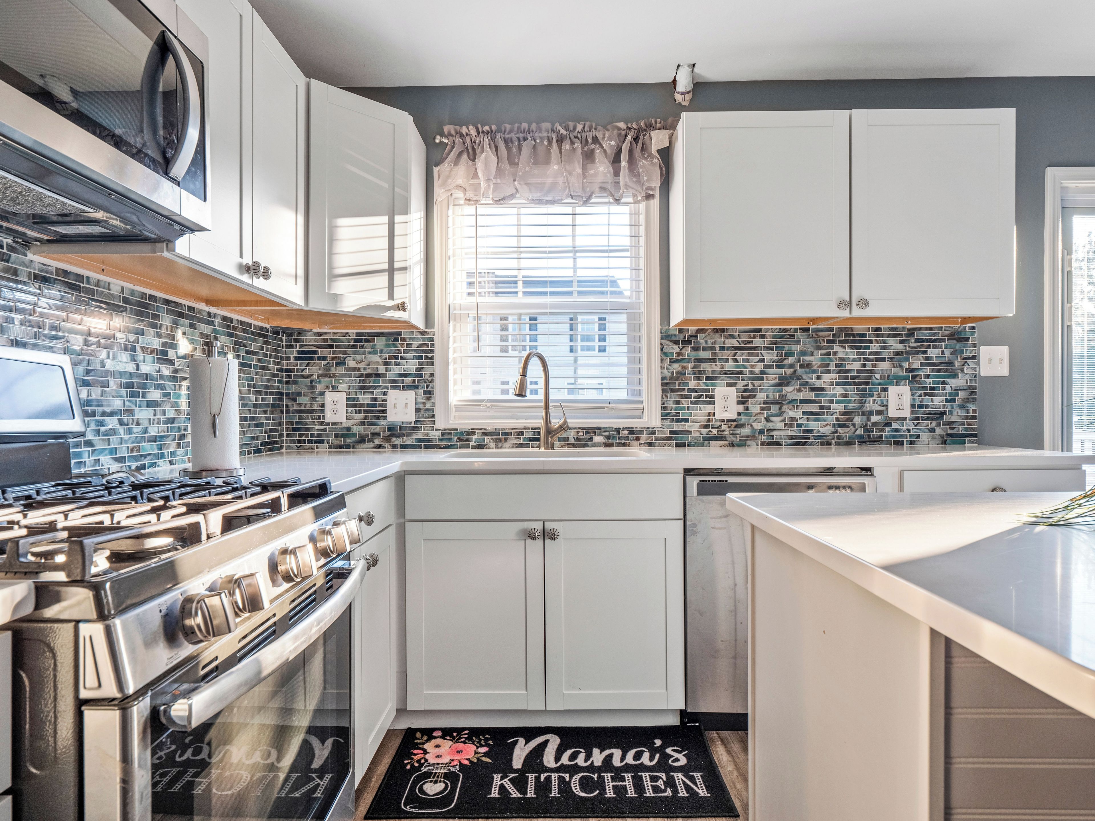 A kitchen with white cabinets, a stainless steel stove, and a window with blinds.