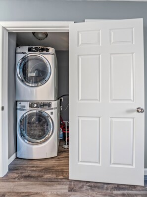 A laundry room with two stacked front-loading washing machines and a closed door. - Valclyde Capitol 2BR Retreat with Balcony & Free Parking (Washington)