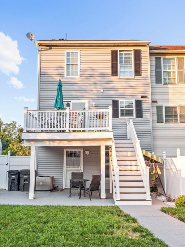 Une maison à deux étages dotée d’un balcon, d’un escalier et d’un petit patio aménagé avec du mobilier d’extérieur.