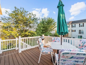 A wooden deck with white railings, a green umbrella, and a white table with floral cushions. - Valclyde Capitol 2BR Retreat with Balcony & Free Parking (Washington)