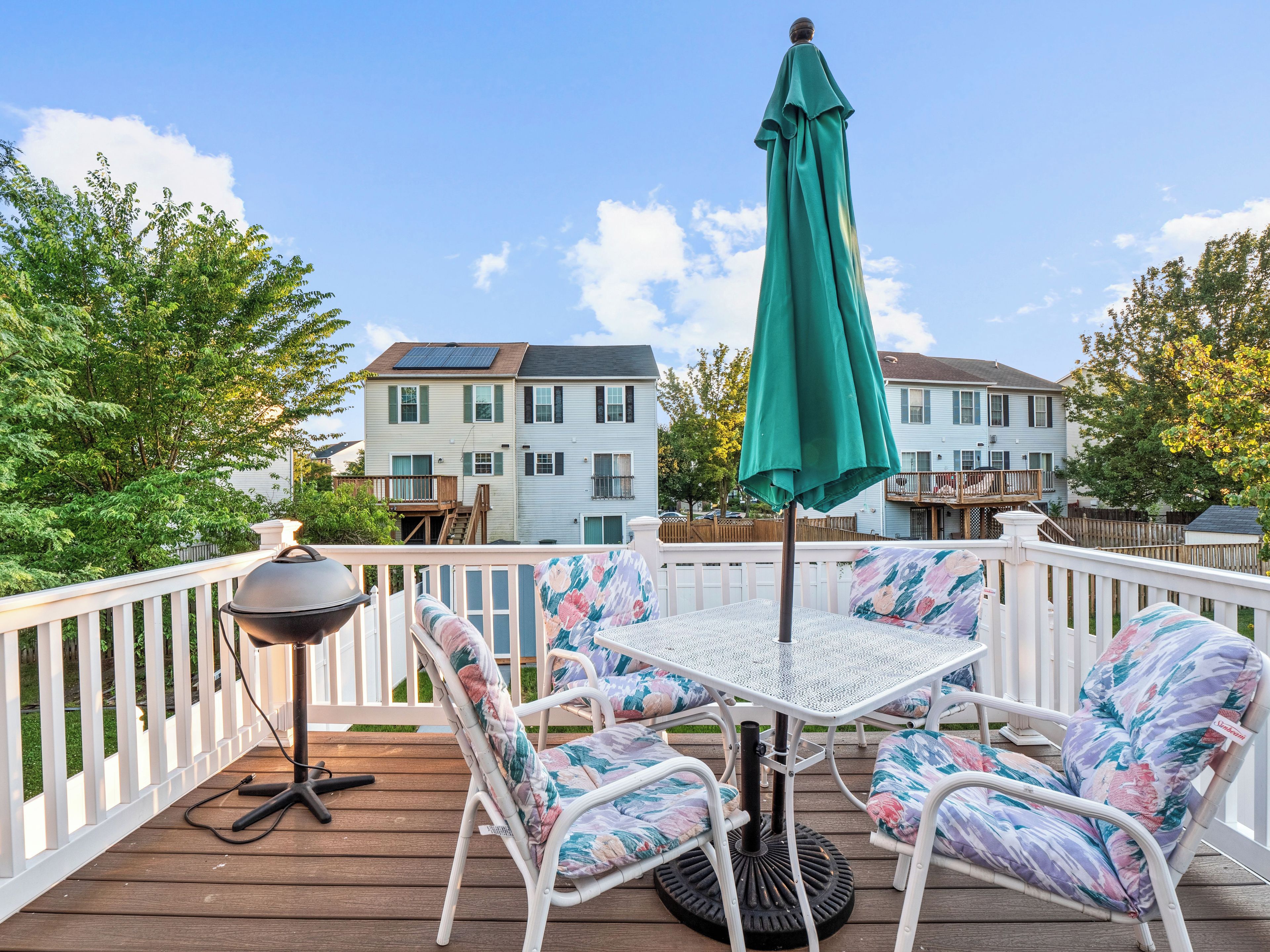 A deck with a table and chairs, a green umbrella, and a lamp.