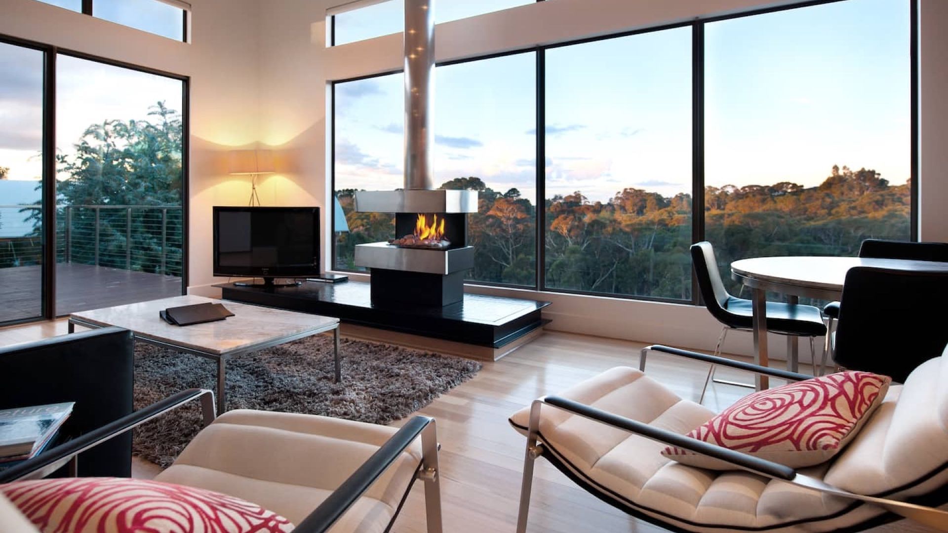 A modern living room with a fireplace, large windows, and a view of the outdoors.
