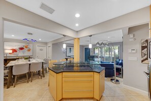 Eine moderne Küche mit Kochinsel, Essbereich mit Stühlen und ein Wohnbereich inklusive Sofa und Fernseher.