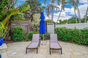 Um pátio com duas cadeiras de descanso, um guarda-sol azul e diversas plantas tropicais.