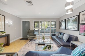 A modern living room with a sofa, armchair, coffee table, and artwork on the walls. - Dolphin Retreat - 4 Bedrooms House with Private Pool (Oakland Park)