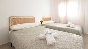 A hotel room with two beds, each with a patterned bedspread and a headboard. There are towels with a logo on them, and a small table with a plant. - Casa Maricarmen Conil de la Frontera by Ruralidays (Cádiz)
