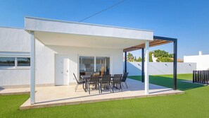 Ein modernes Haus mit einer überdachten Terrasse, ausgestattet mit einem Esstisch und Stühlen.