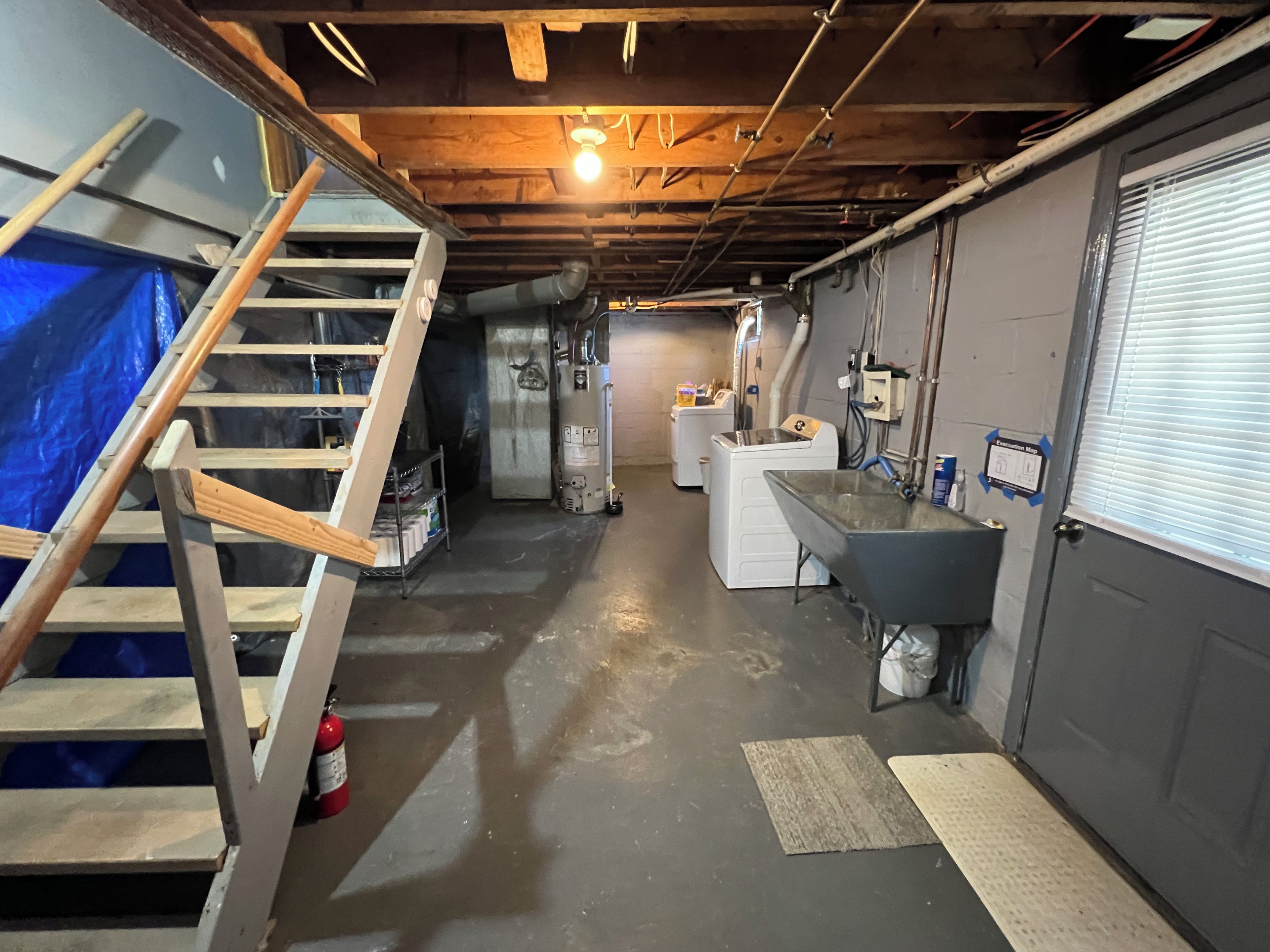 A basement with a wooden ladder, a washing machine, a sink, and a fire extinguisher.