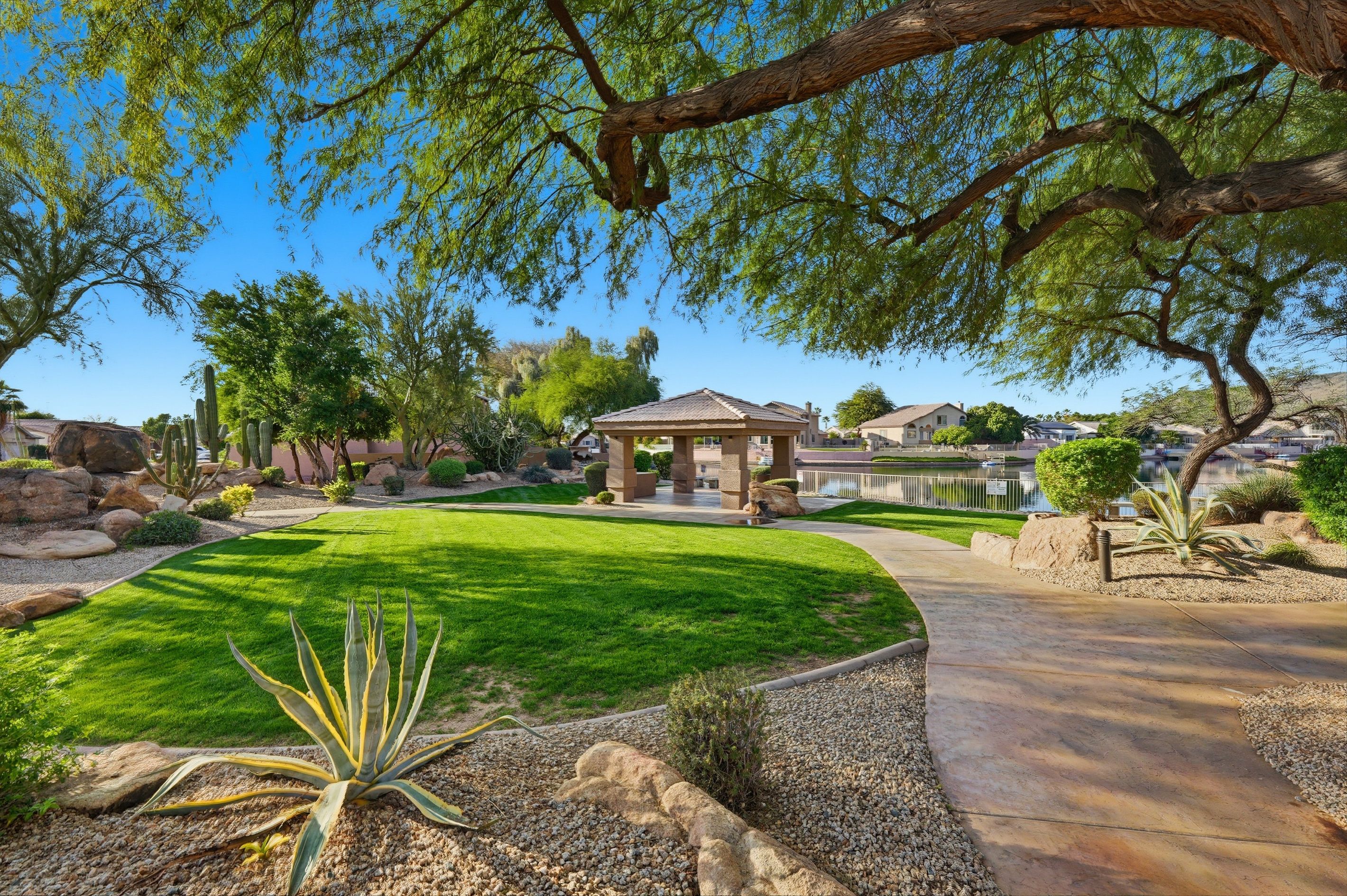 Ein gepflegter Garten mit einem Pavillon, blauem Himmel und Häusern im Hintergrund.