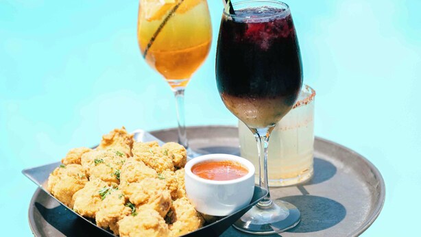 Una bandeja con comida frita, una bebida con pajita y un vaso de refresco rojo junto a una piscina.