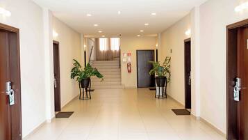 A hotel hallway with two potted plants, a staircase, and a fire extinguisher.