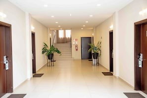 A hotel hallway with two potted plants, a staircase, and a fire extinguisher.