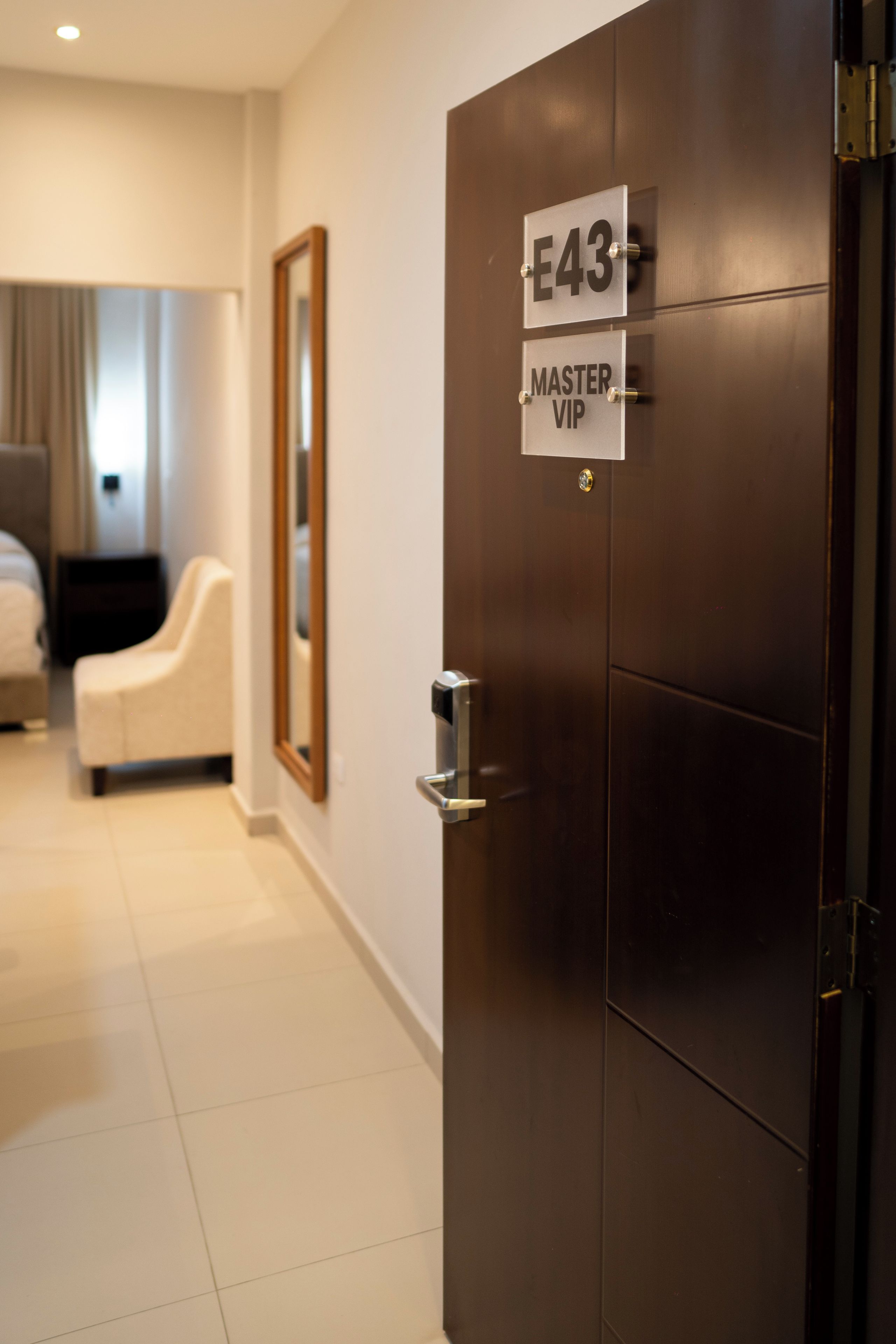 Habitación de hotel con una puerta de madera oscura, un cartel que indica el número de habitación E43 y una etiqueta que dice 'MASTER VIP'.