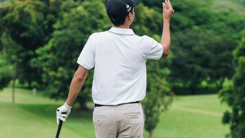 Una persona con camisa y pantalones cortos en un campo de golf, con un palo de golf en mano, apuntando a una pelota.