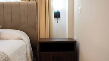 A bedroom with a bed, a nightstand, a wall-mounted light, and a window with curtains.