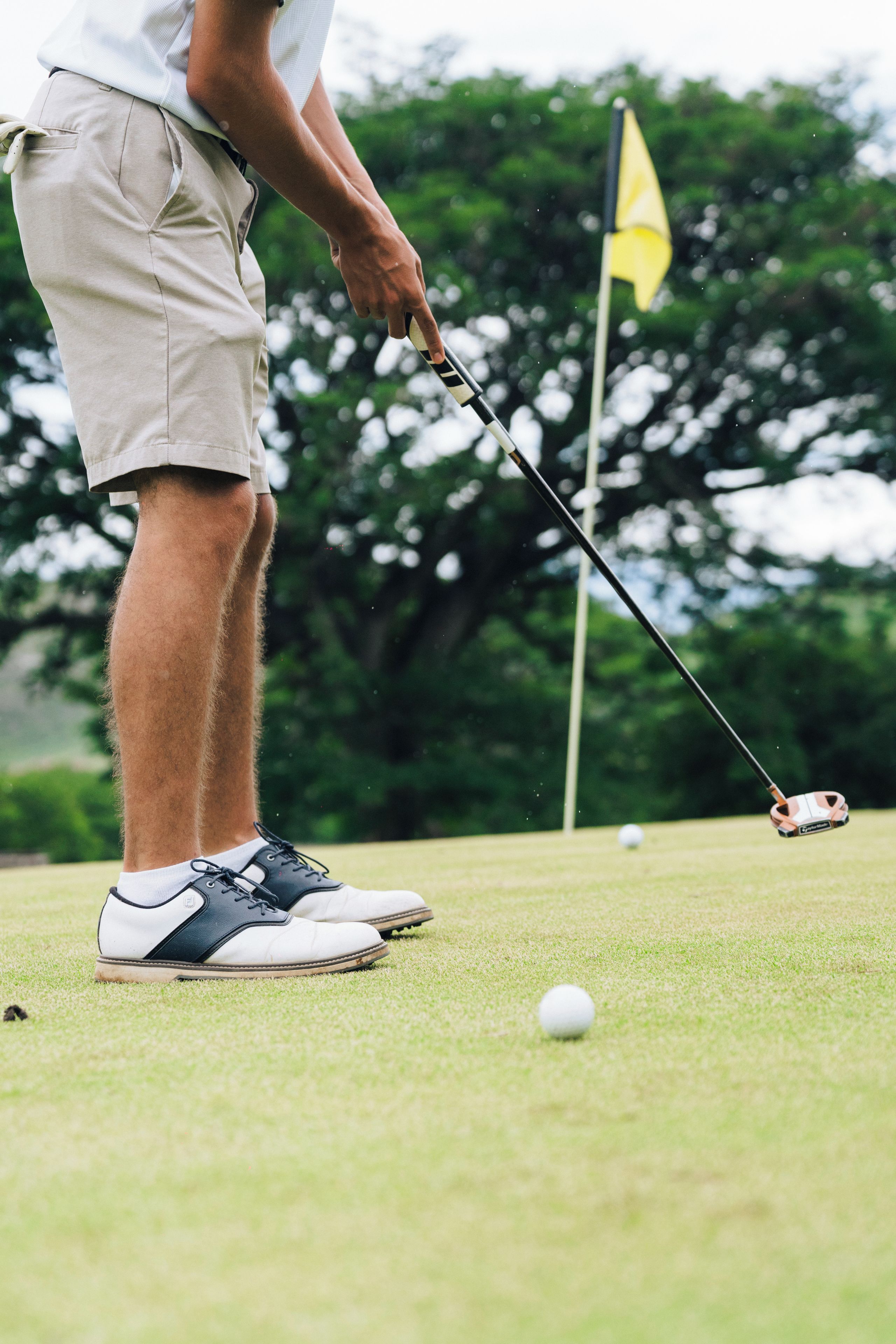 Una persona con pantalones cortos y camisa blanca a punto de colocar una pelota de golf en un campo de prácticas.
